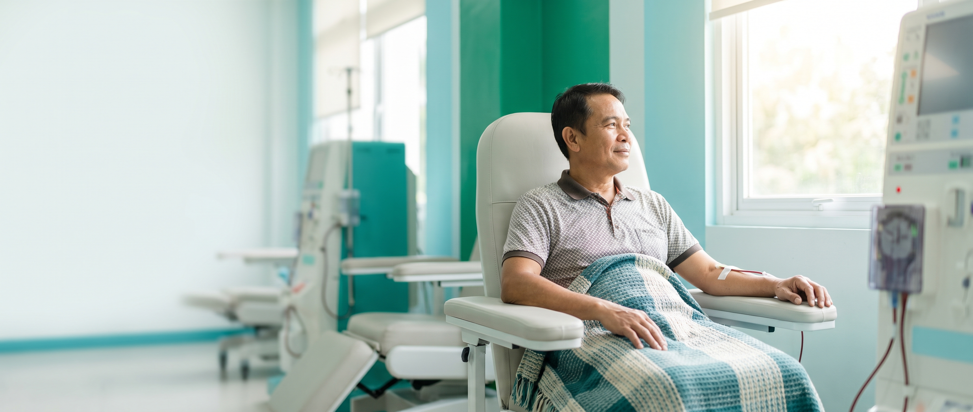 A dialysis patient seated by a bright window in a modern Philippine center, looking out with quiet hope